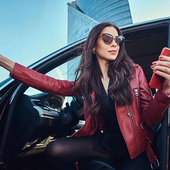 Coton Lederreinigung - stylische Frau mit roter Lederjacke steigt aus Auto