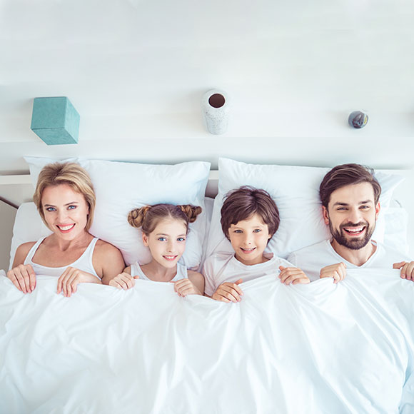 Coton Textilreinigung - Reinigung Bettwäsche - Familie in kuscheligem Bett